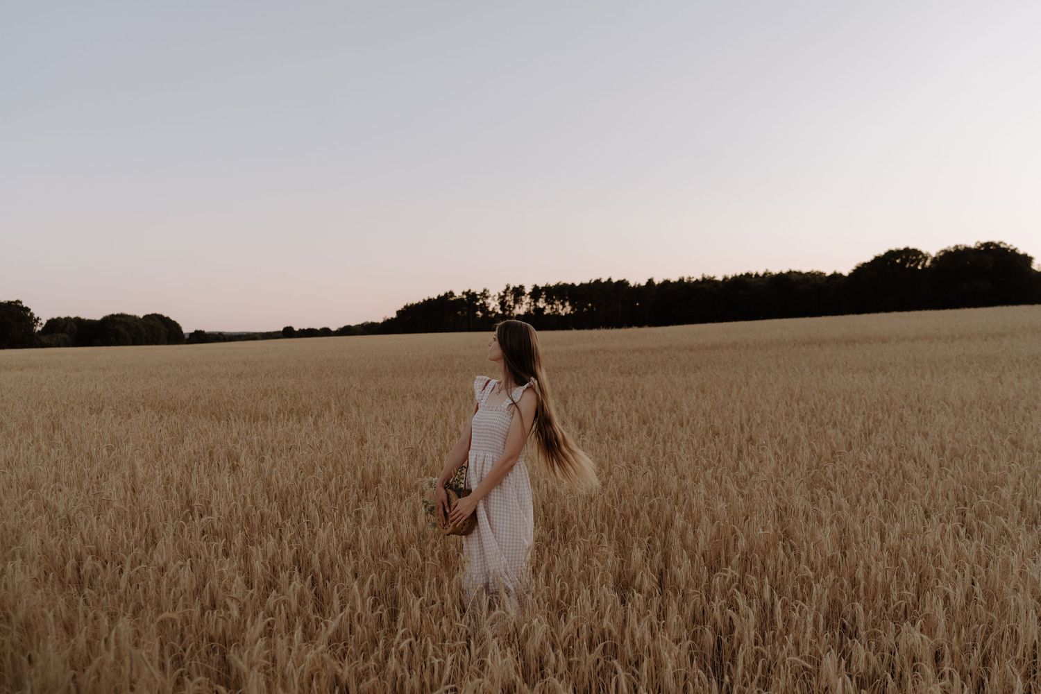 A figure in a flowing white dress stands among golden wheat fields at dusk.