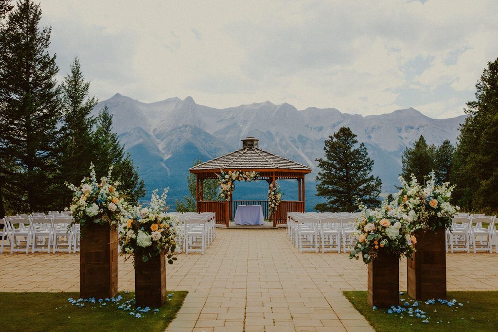 Stunning mountain wedding venue with white chairs and floral arch overlooking lake and peaks.