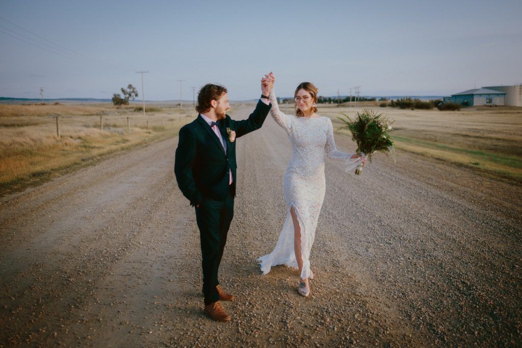 Joyful couple celebrating on a dirt road in formal wedding attire.
