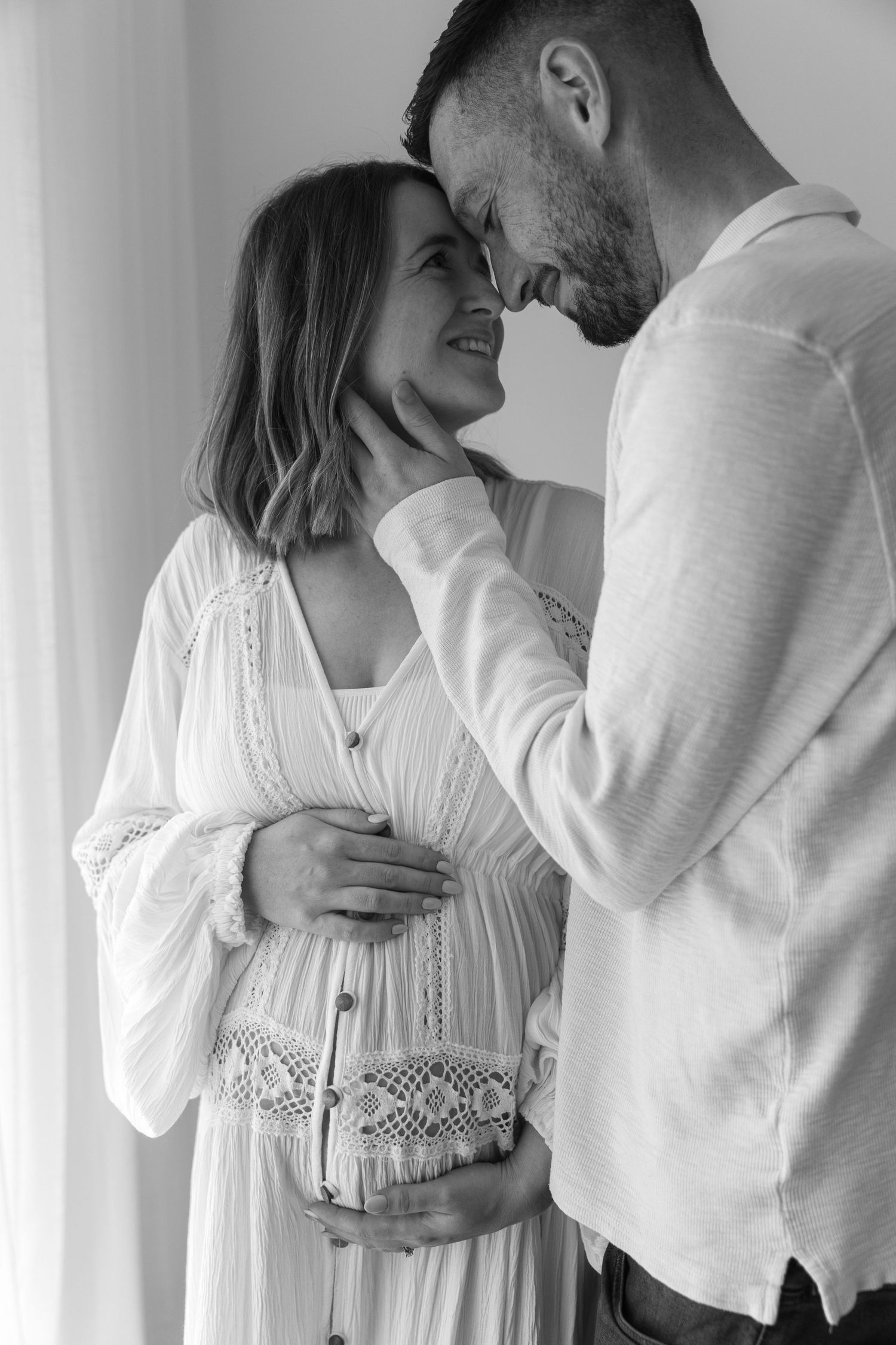 Black and white portrait of loving couple sharing tender moment in white attire.