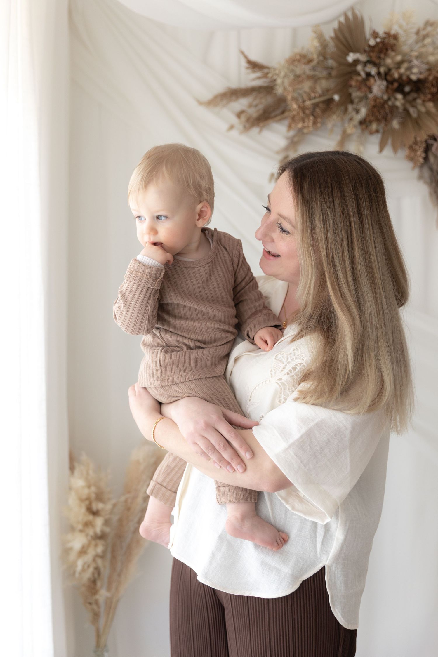 Tender moment between caregiver and baby against wall with dried floral decoration.