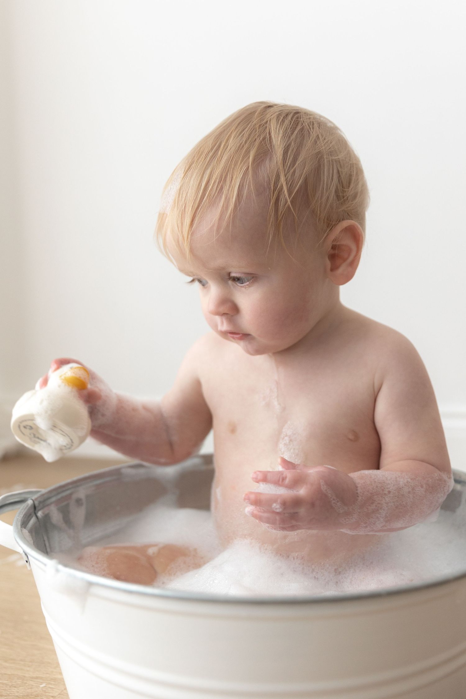 Toddler playing in bubble bath with white metal tub.