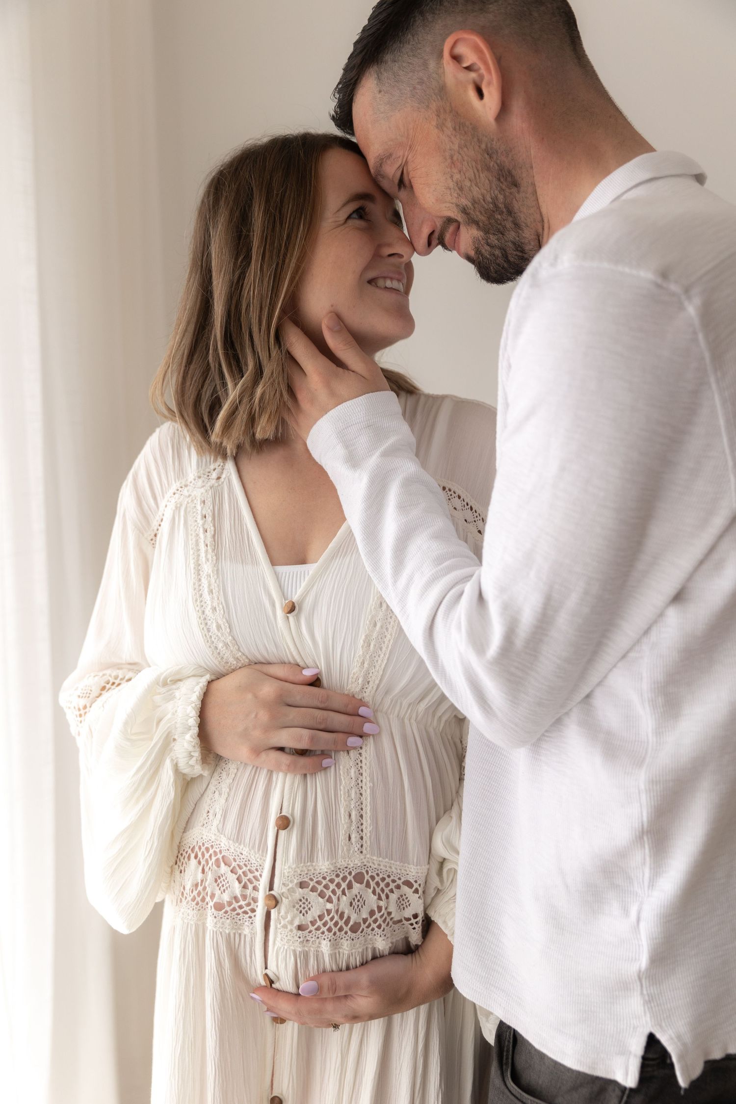 Romantic maternity portrait of couple in white clothing sharing an intimate moment.