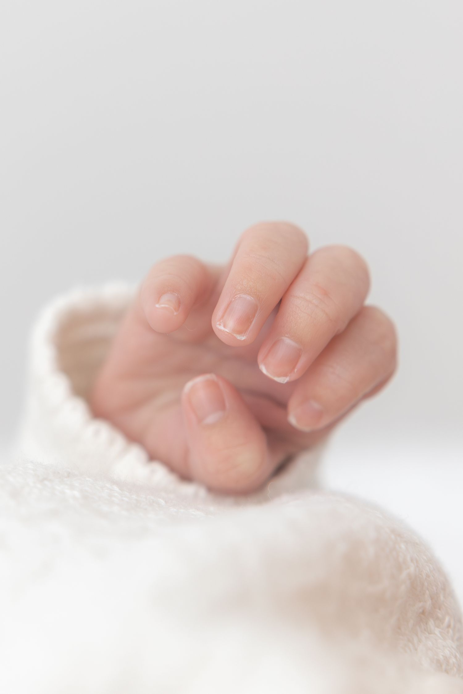 Close-up of tiny baby hand with delicate fingernails against white fabric.