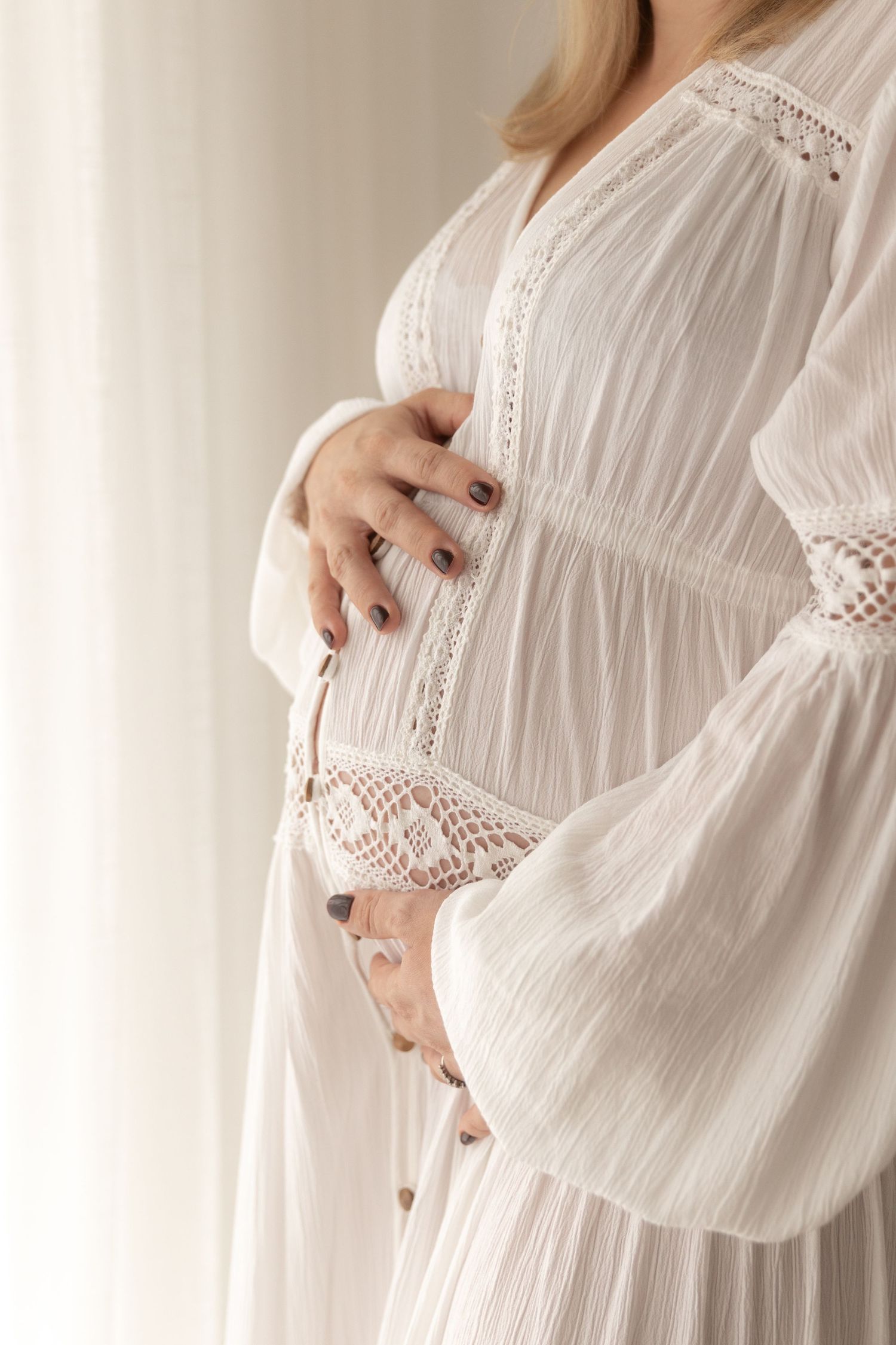 Delicate white lace maternity dress with flowing sleeves highlighted against light background.