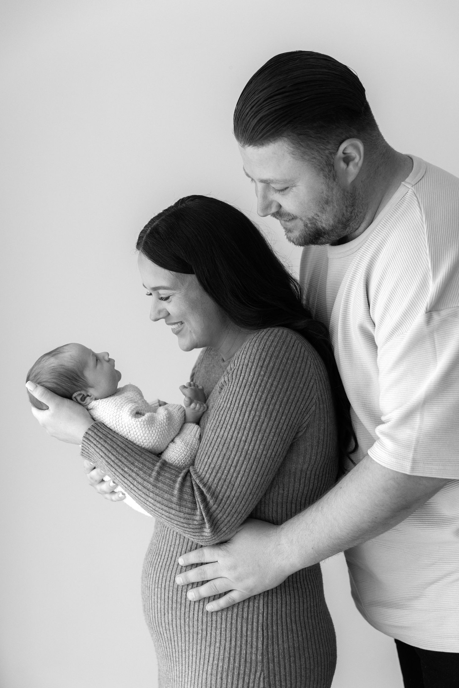 Black and white portrait of parents lovingly looking at their newborn baby in an intimate family moment.