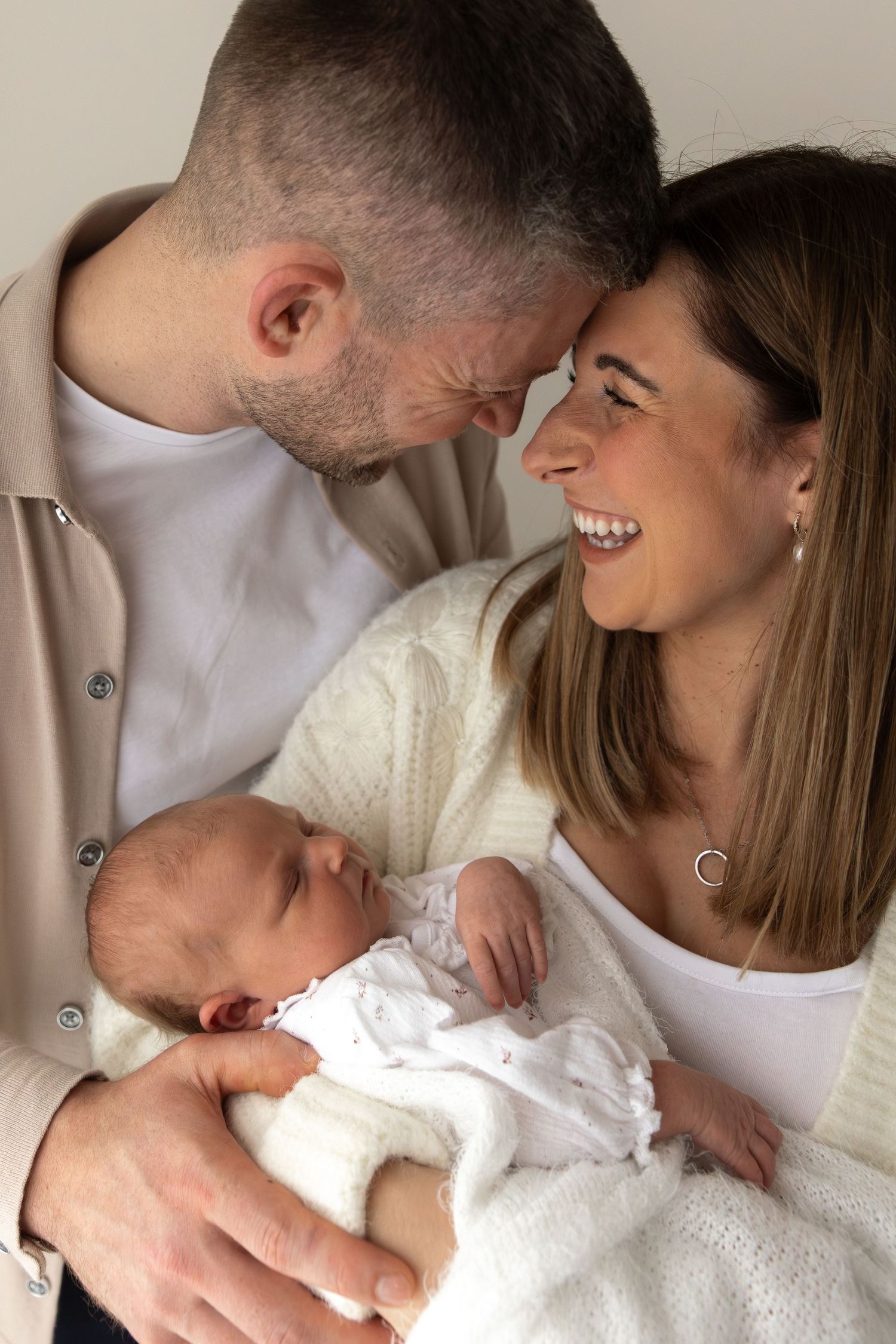 Happy couple sharing intimate moment with their newborn baby dressed in white.