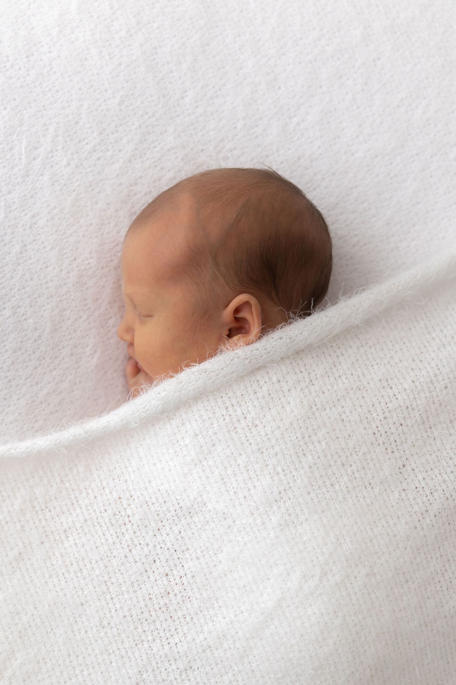 Profile view of sleeping baby nestled in soft white blanket.
