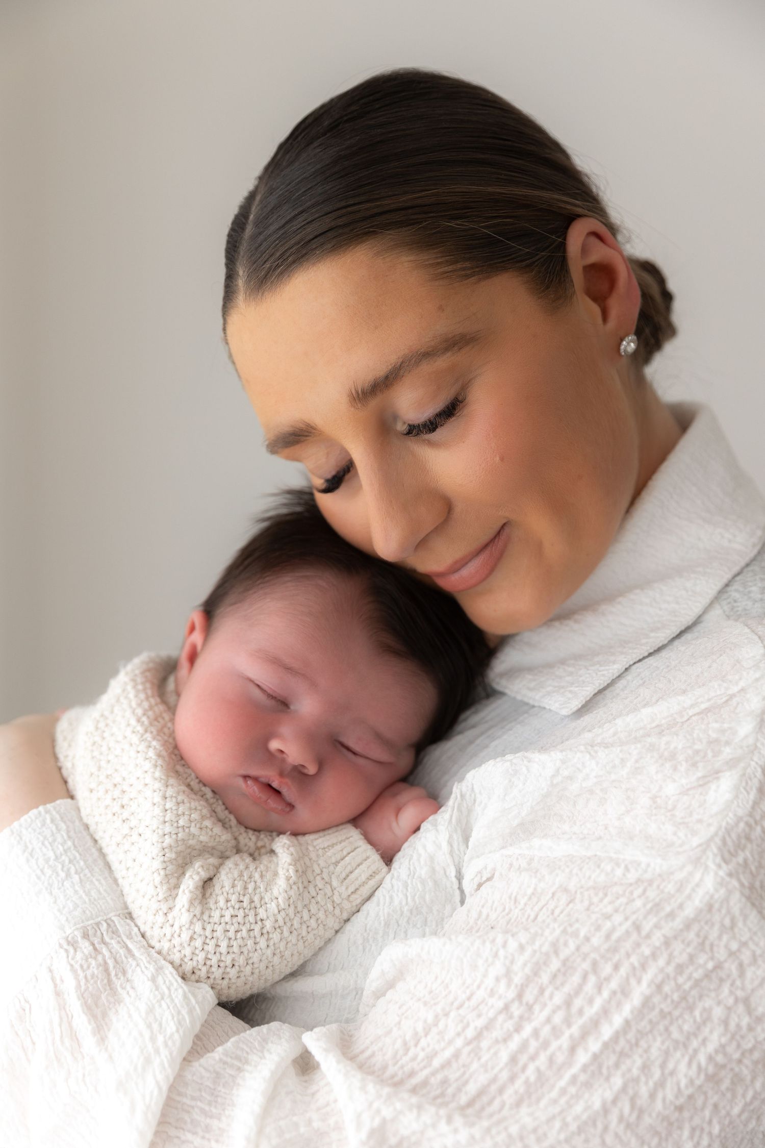 Peaceful portrait of sleeping newborn cuddled against parent in white attire.