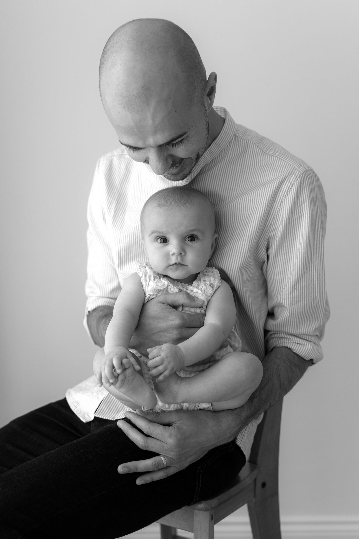 Tender black and white portrait of parent holding infant in white outfit.