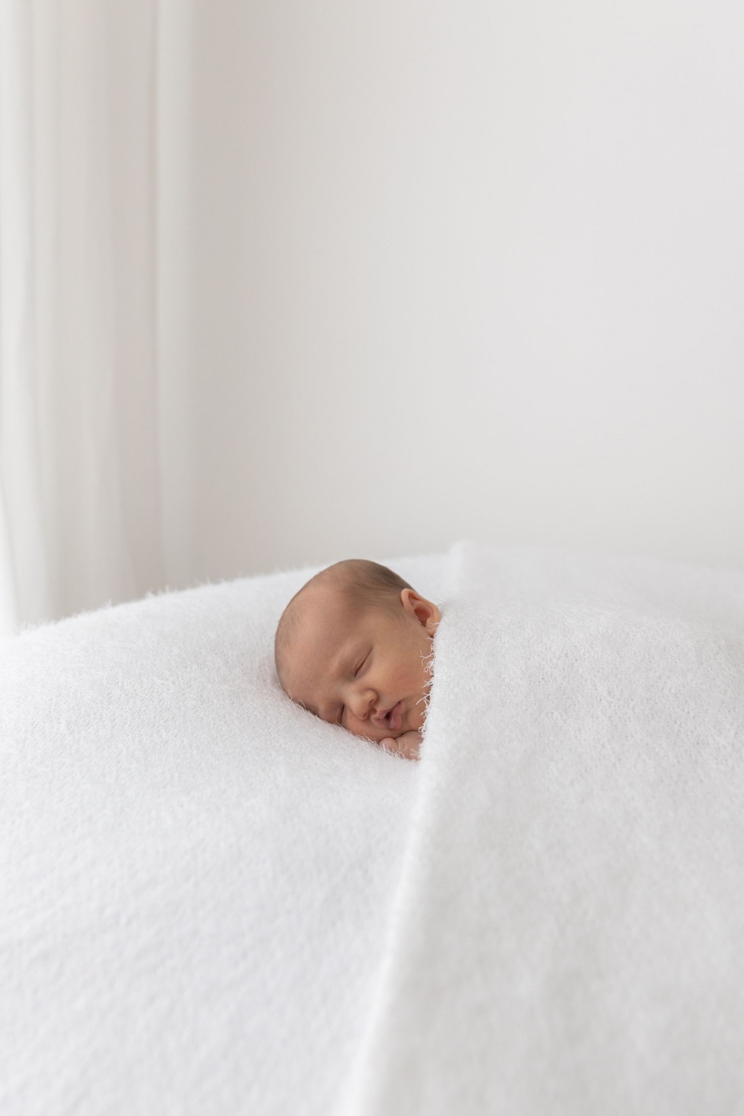 Sleeping newborn's head peeking out from white textured blanket.