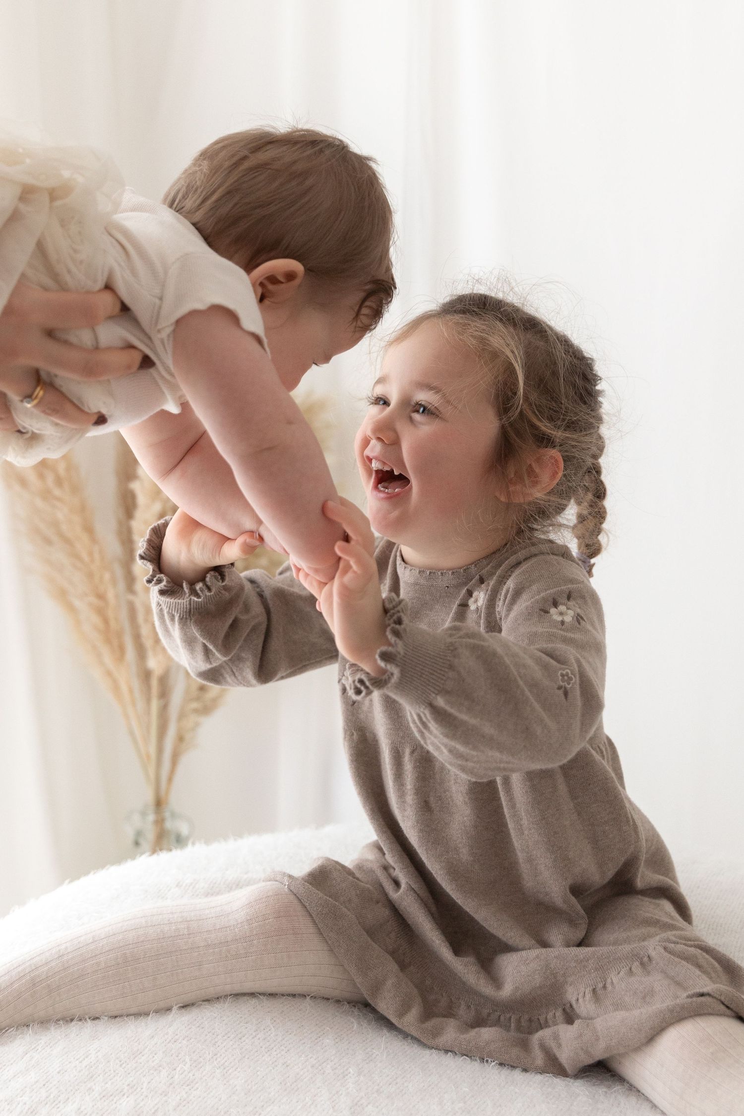 Two children playing and laughing together on white surface.