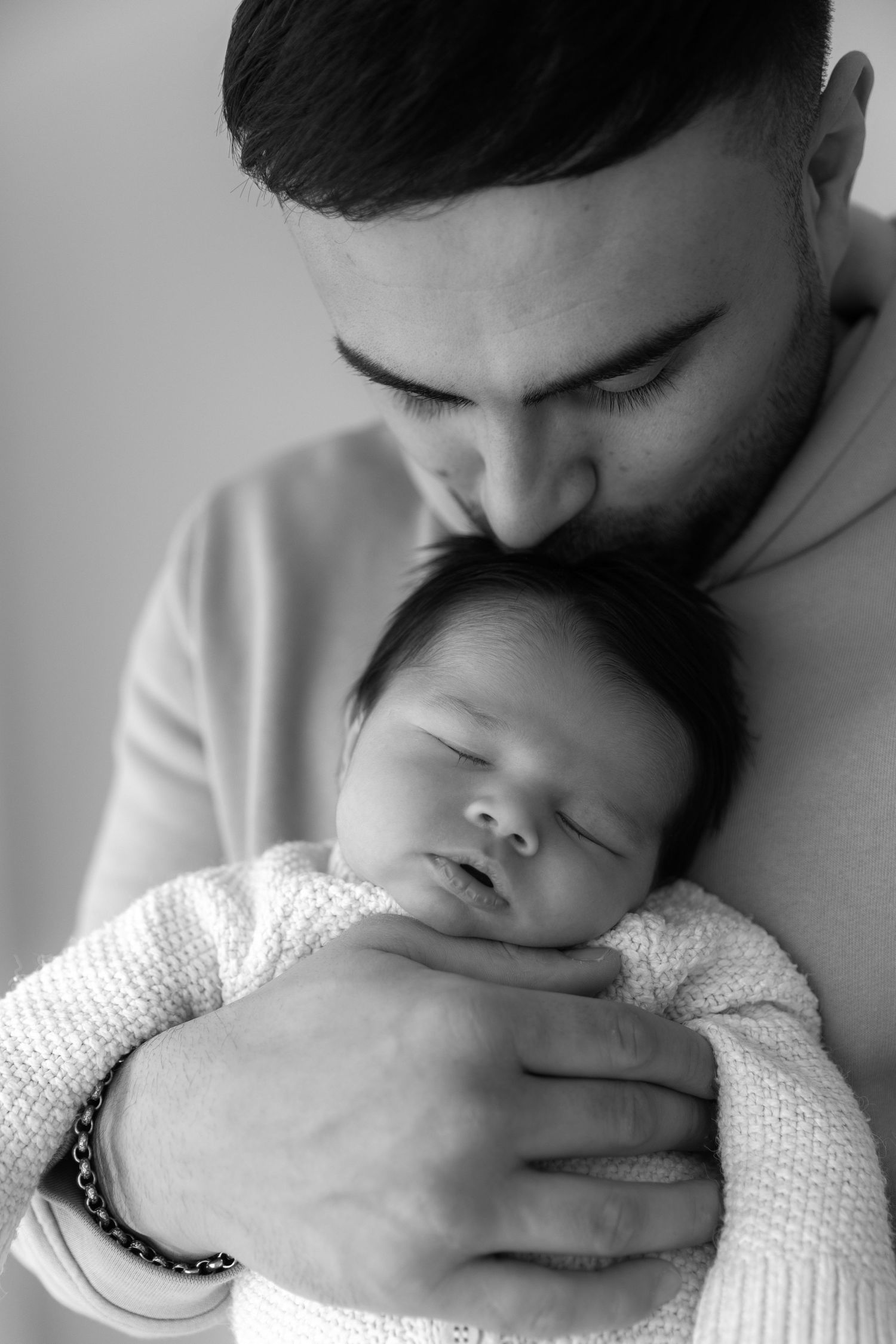 Black and white portrait of tender moment between parent and sleeping newborn in white sweater.