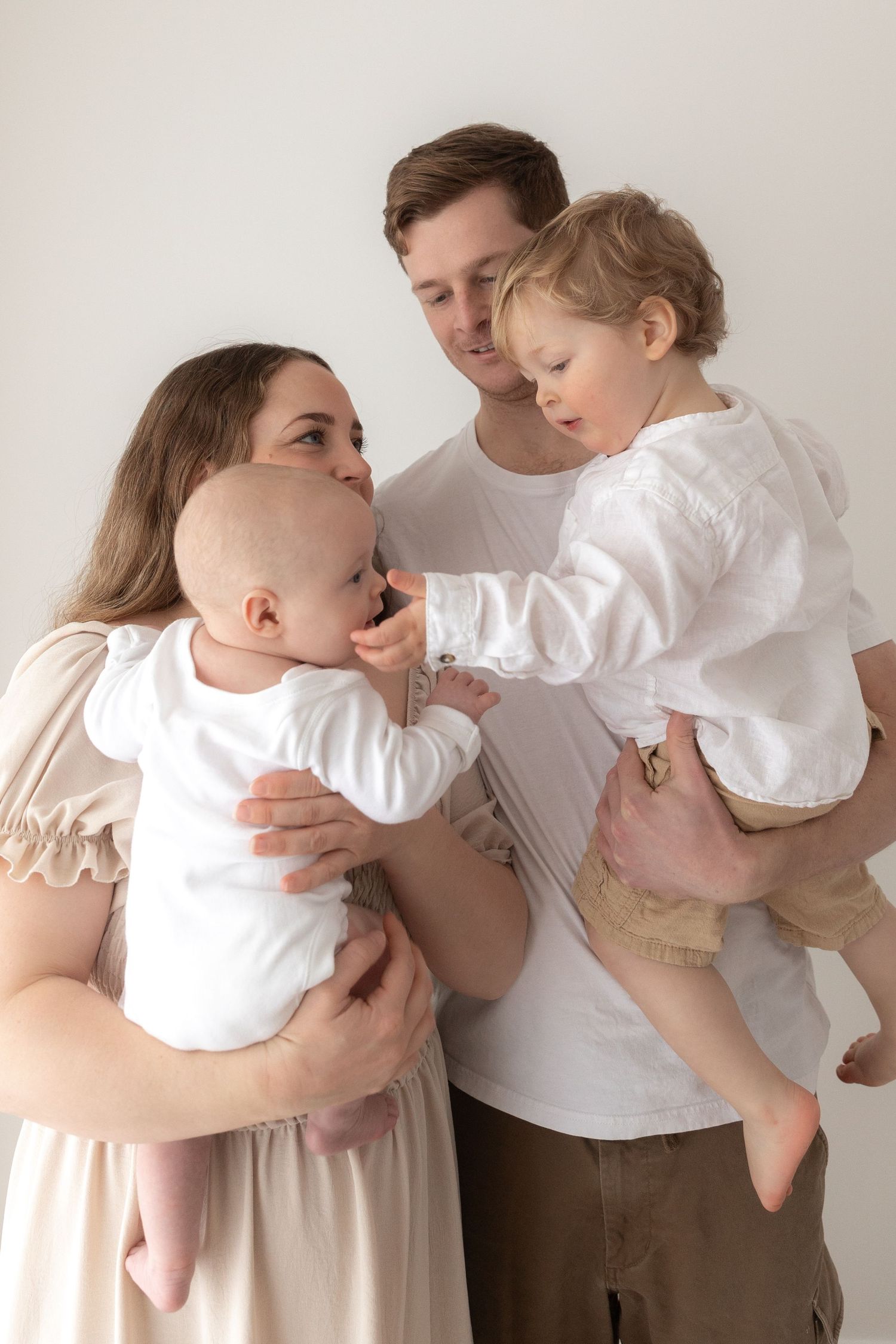 Family wearing white clothes sharing intimate moment against neutral background.