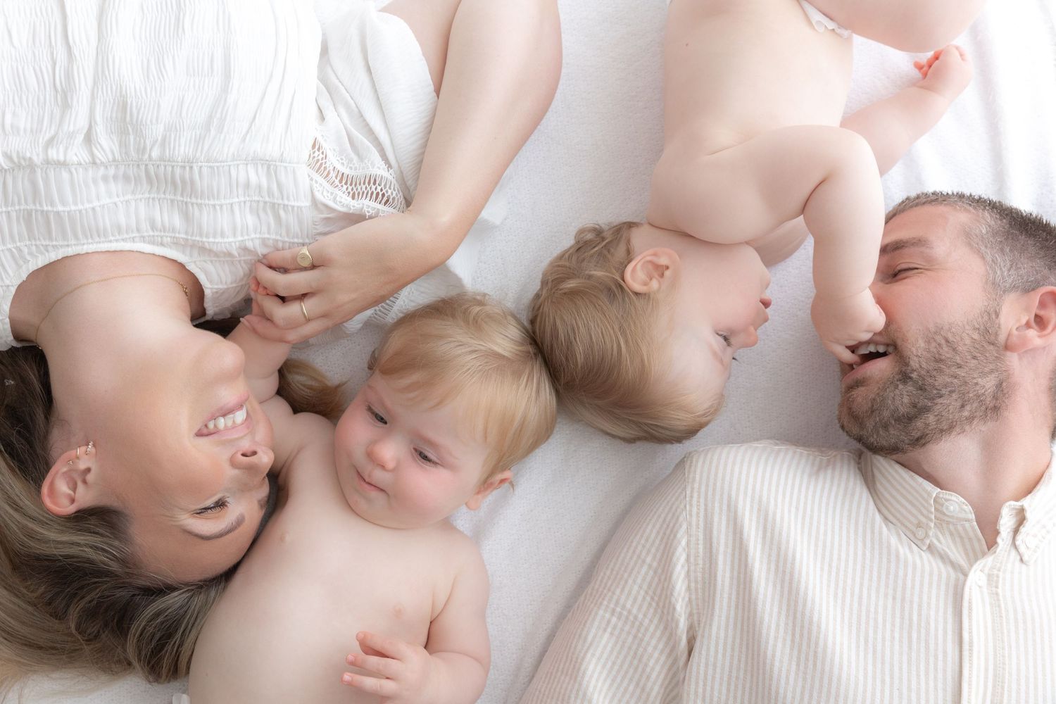 Family lying together on white bedding sharing intimate moment.