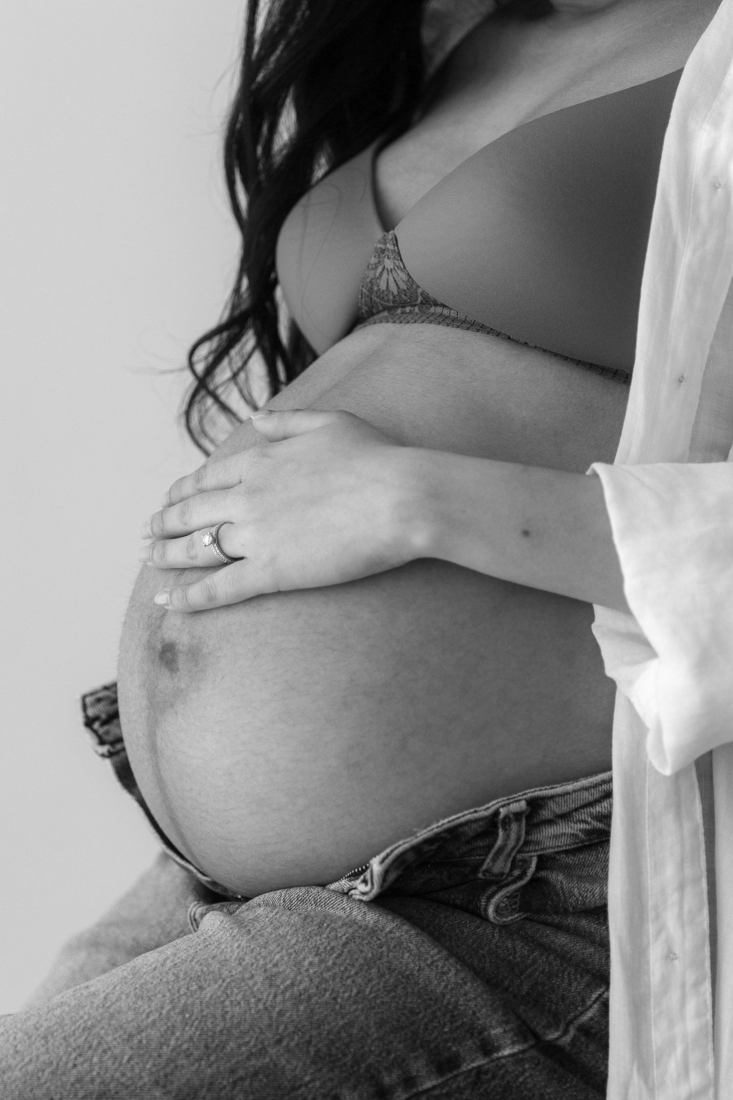 Black and white closeup of pregnant belly with hands gently resting on bump.