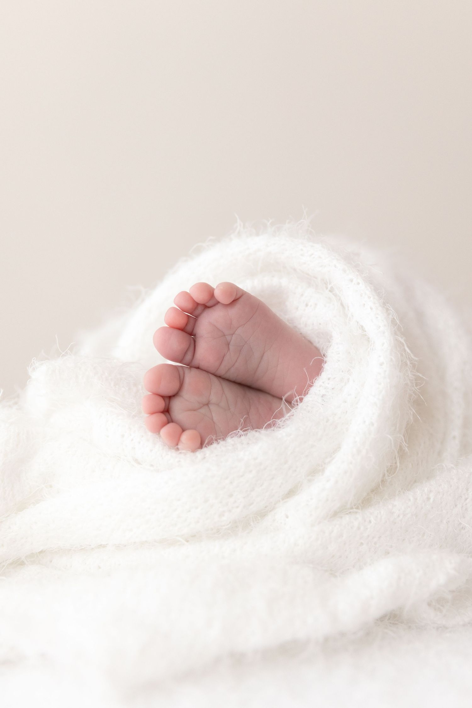 Tiny baby feet peek out from soft white blanket in high key photography.