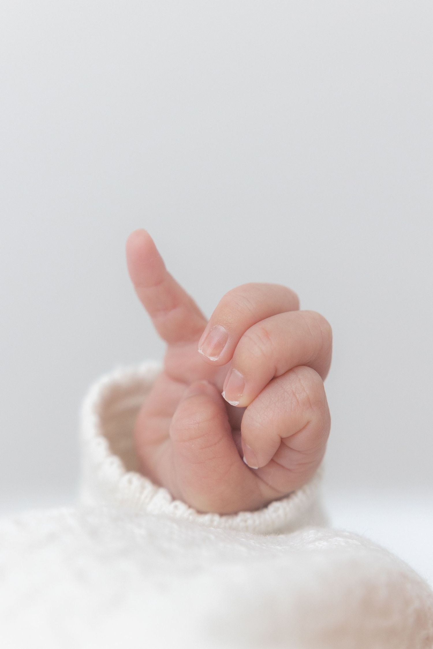 Close-up of tiny baby hand emerging from white knitted fabric.