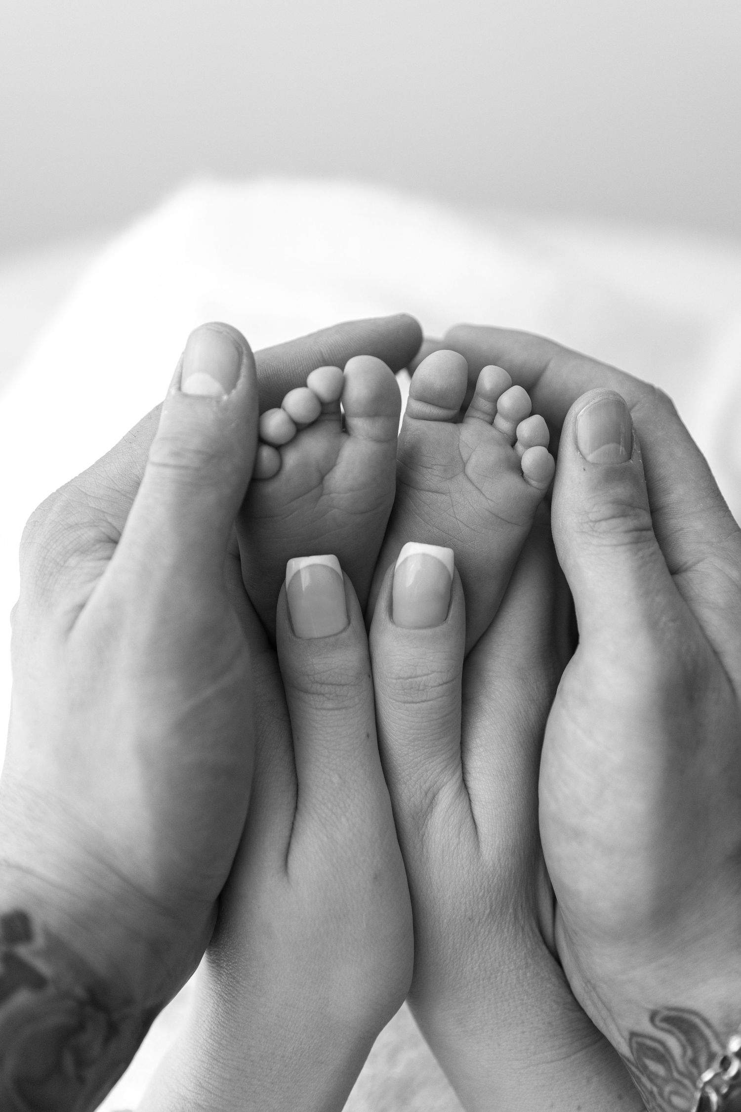 Black and white close-up of hands cradling tiny baby feet against white background.