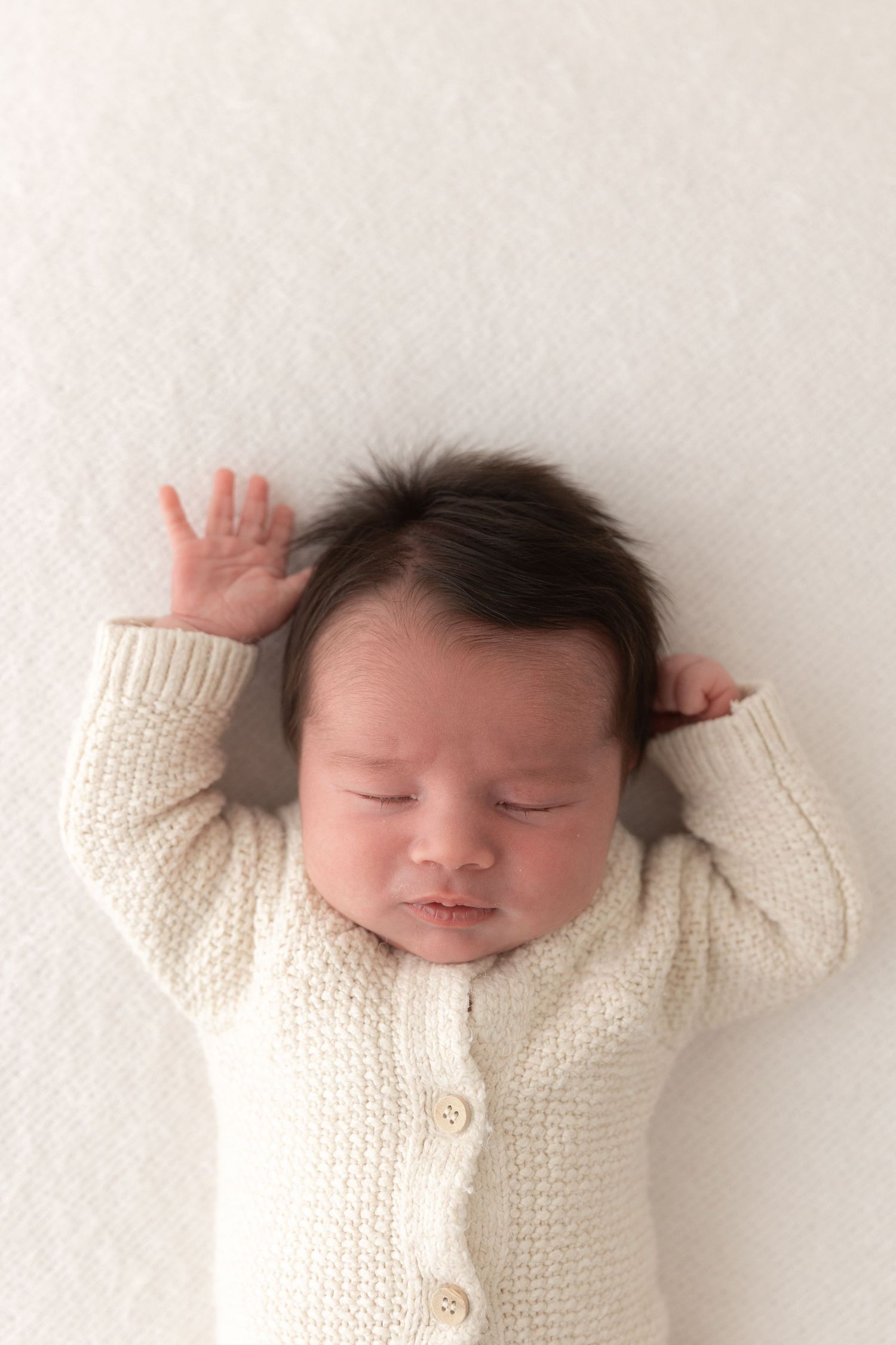 Peaceful sleeping baby wearing cream knit cardigan lies on white background.