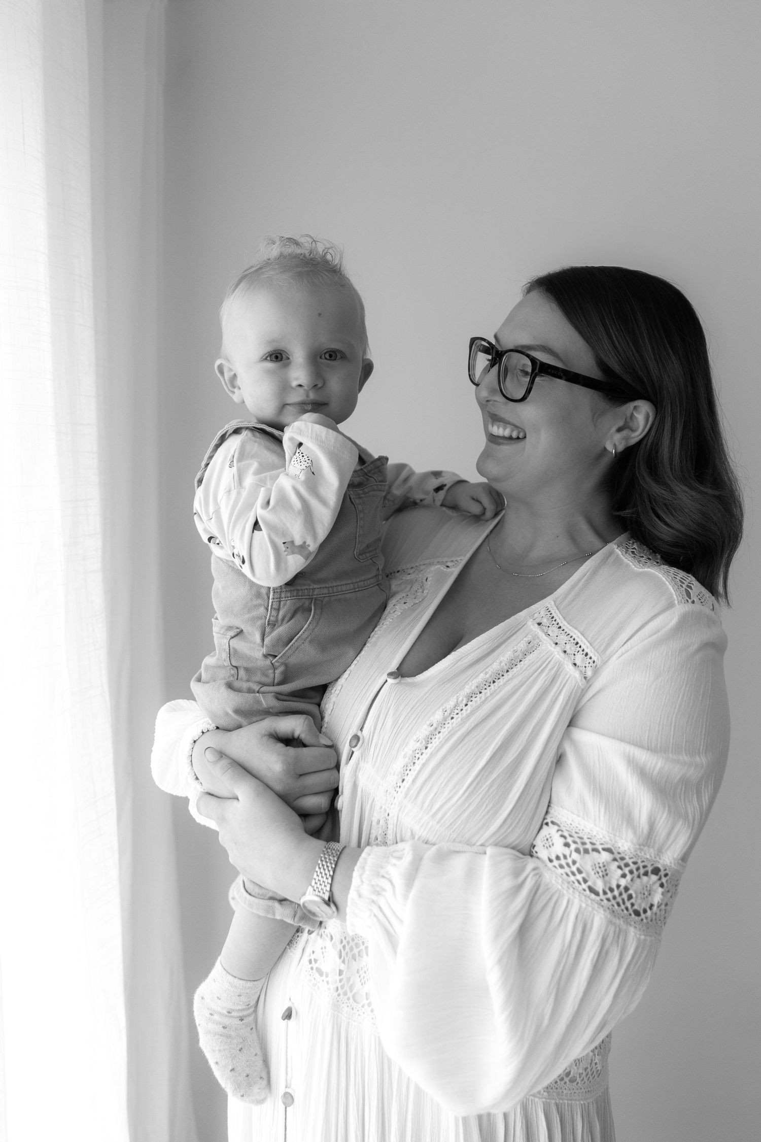 Sweet moment between child and caregiver in white dress against light wall.