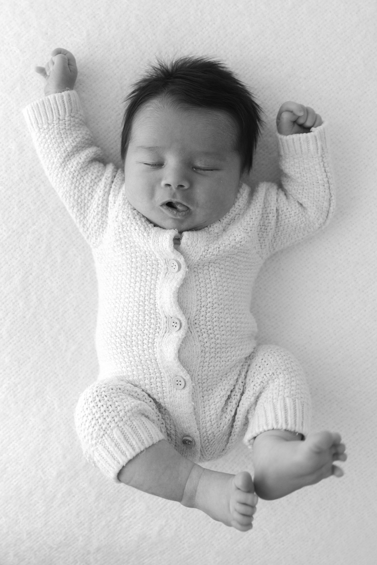 Sleeping infant in white knitted cardigan onesie against white background.