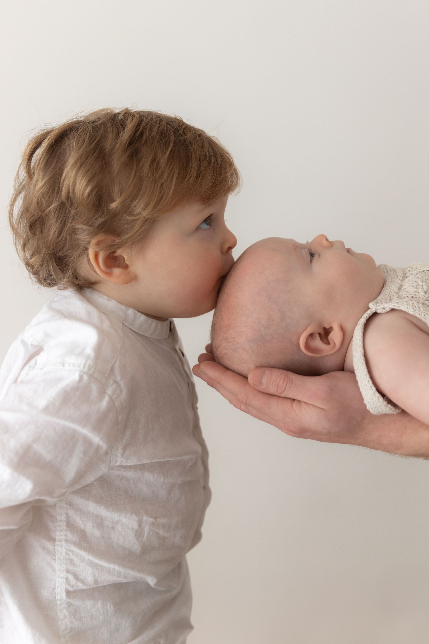Sweet moment between siblings in white against light background.