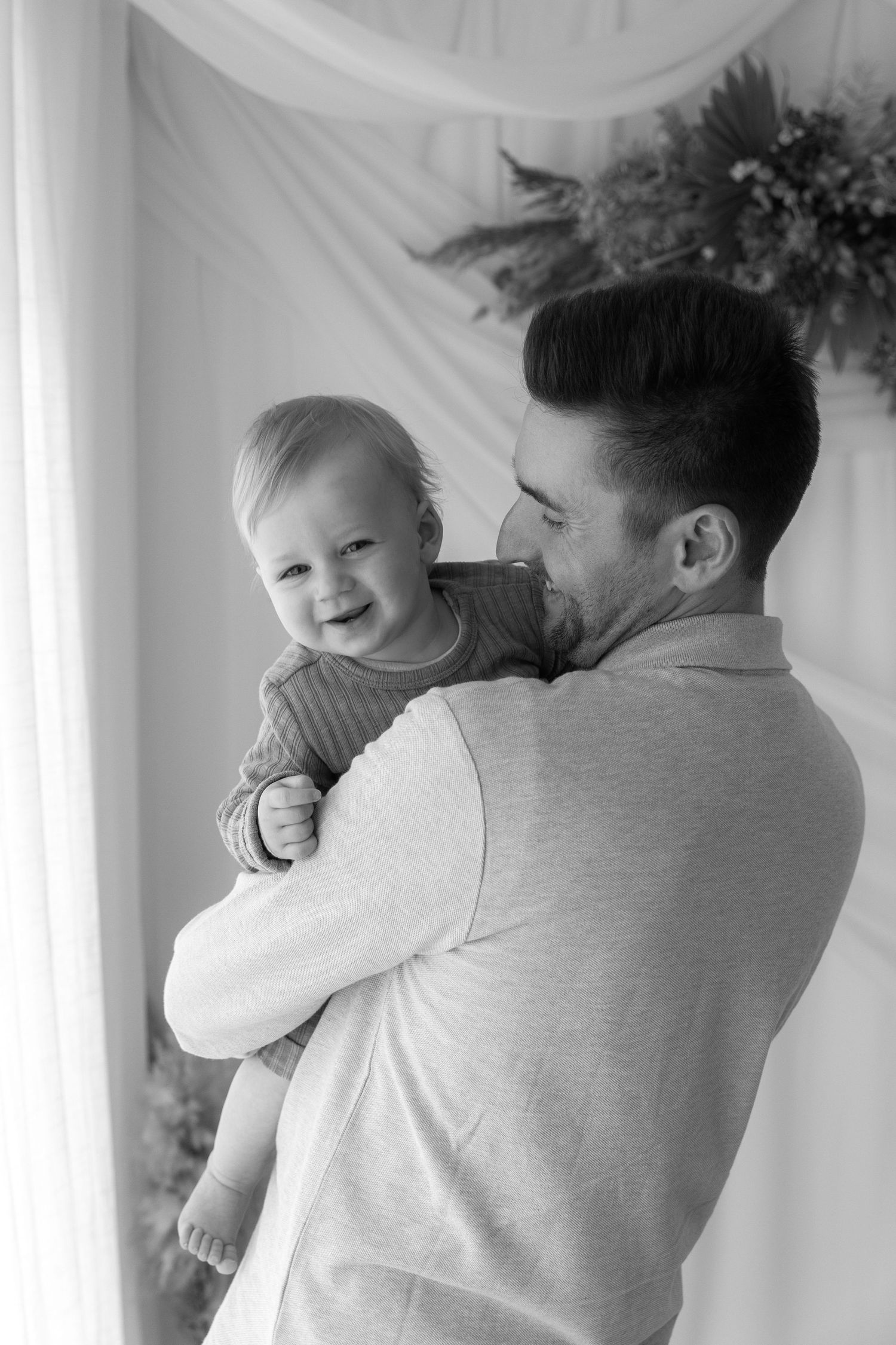 Sweet candid moment of an infant smiling while being held in monochrome portrait.