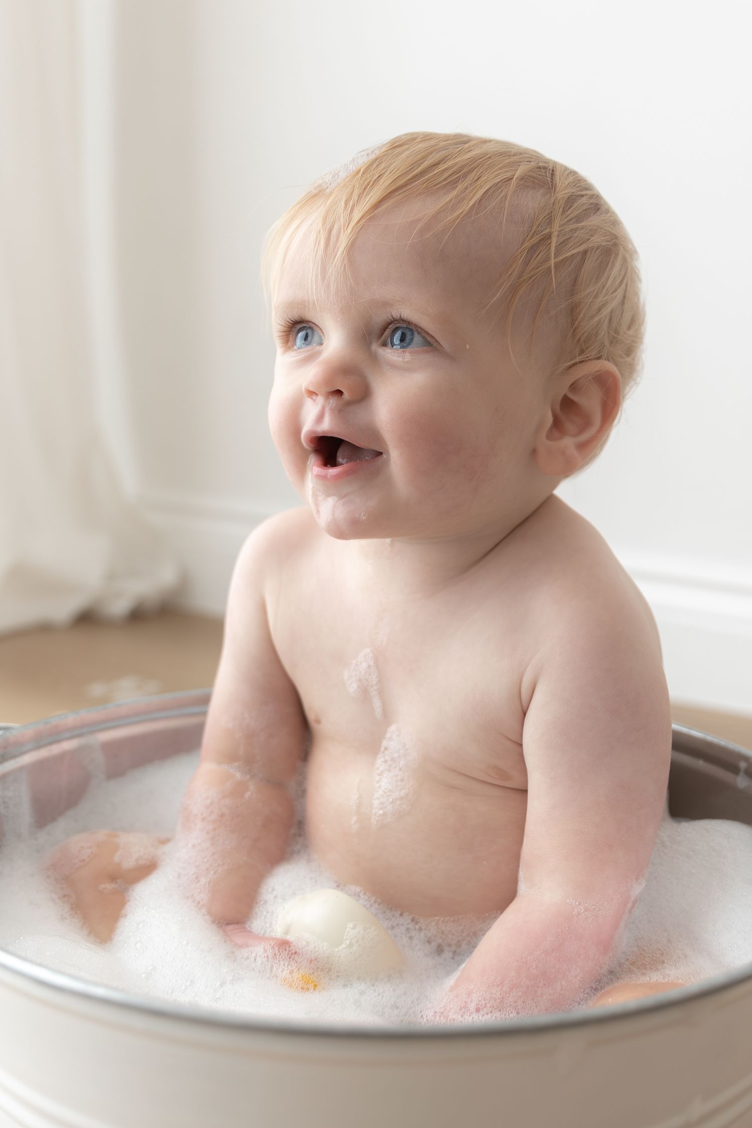 Joyful baby enjoying bath time in metal tub with bubbles.