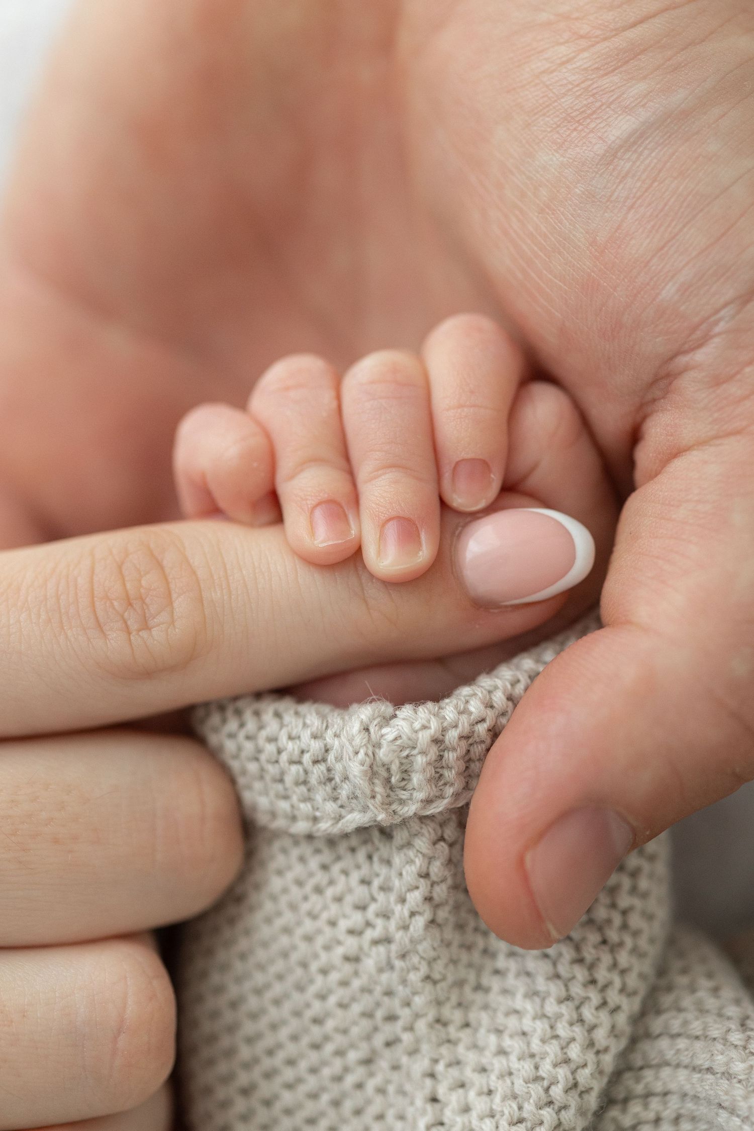 Close-up of tiny baby fingers grasping adult hands against soft knitted fabric background.