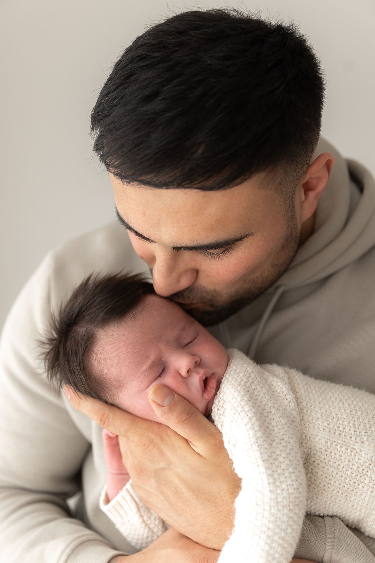 Tender moment between parent and sleeping newborn wrapped in white knitted blanket.