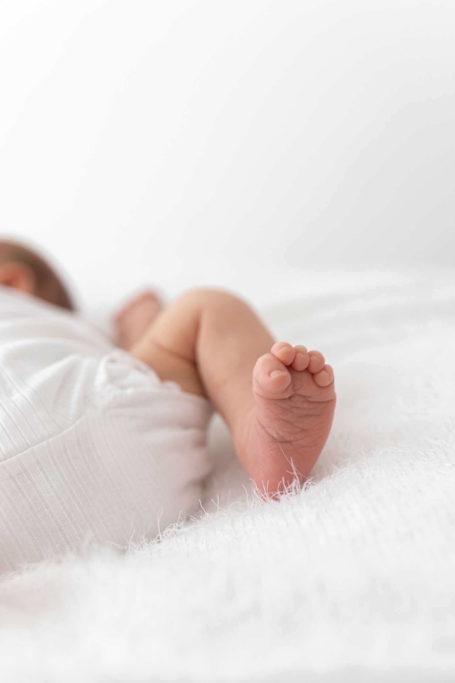 Close-up of tiny baby foot resting on white textured blanket.