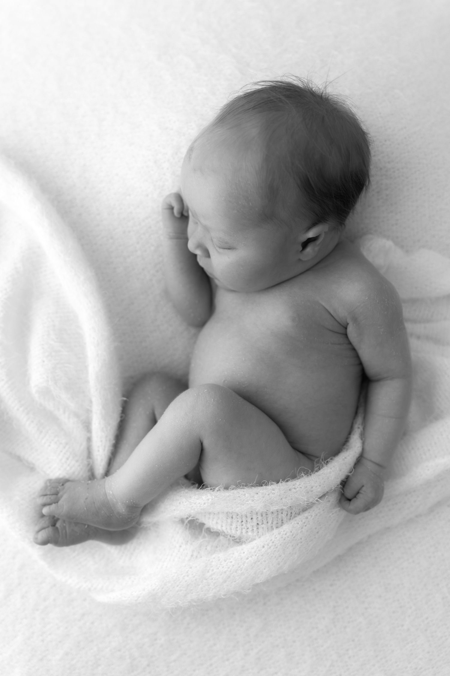 Sleeping newborn wrapped in white textile captured in black and white.