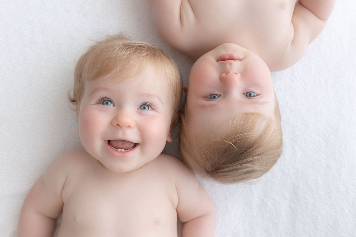 Two babies lying together on white background sharing joyful moment.
