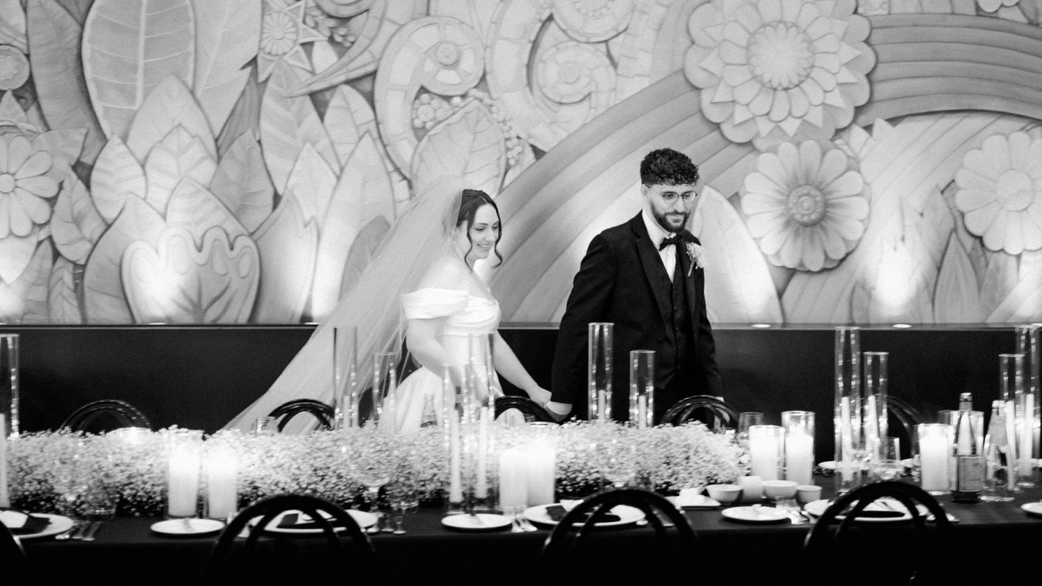 Black and white photo of bride and groom standing at elegantly decorated wedding reception table with candles.