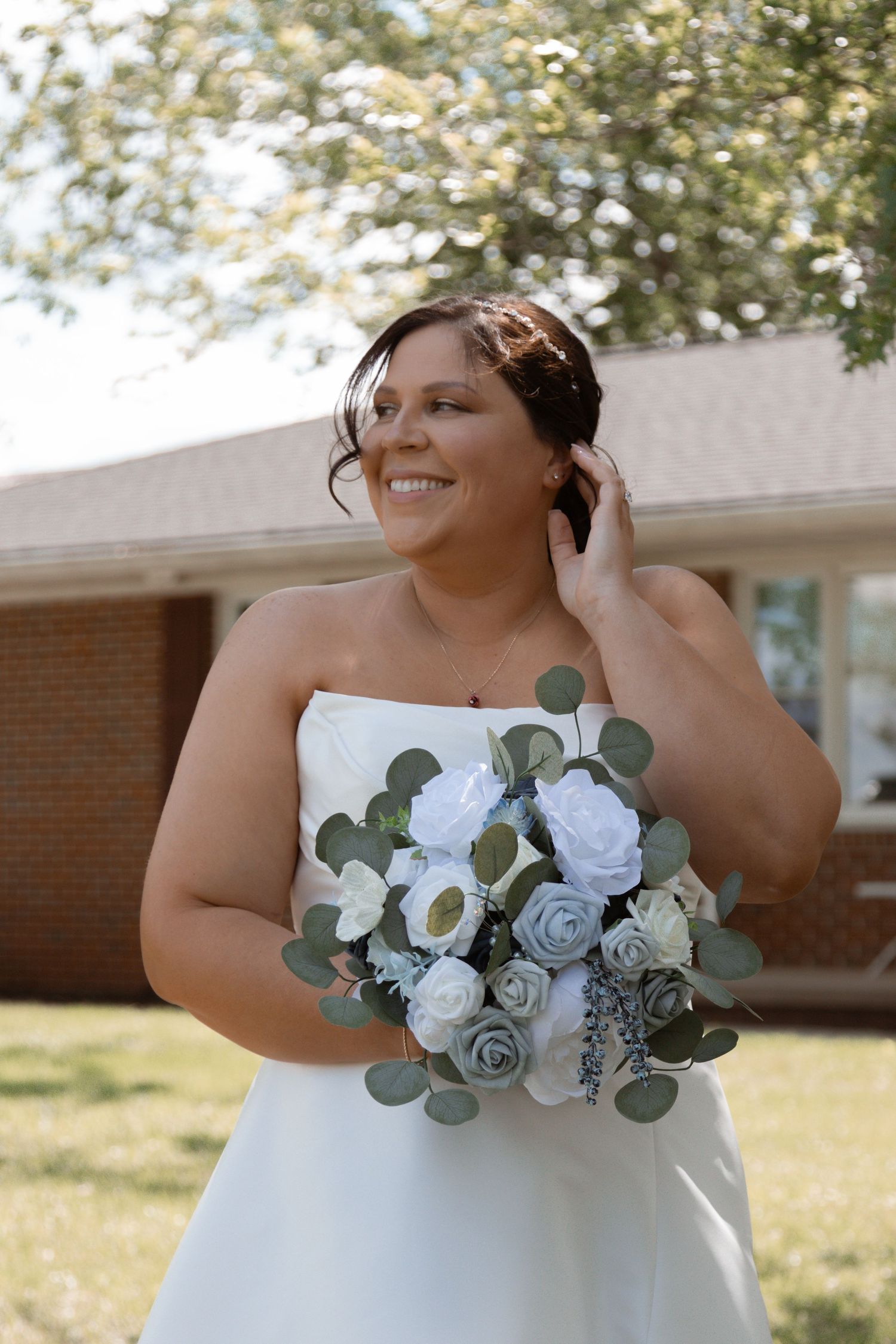 A bride holds a beautiful bouquet of white and dusty blue roses with eucalyptus leaves against her white wedding dress.