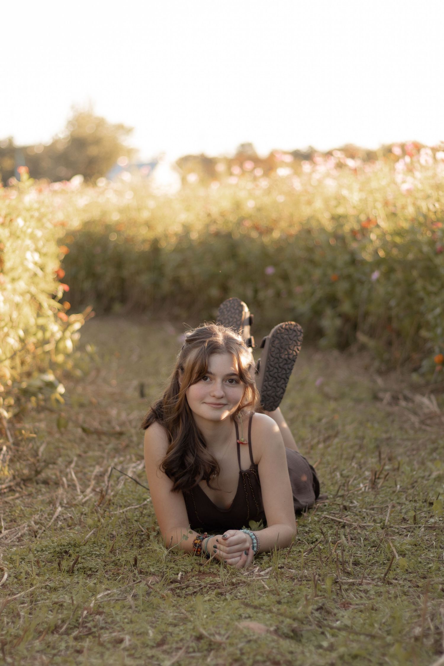 Young woman lying in a grassy field surrounded by wildflowers during golden hour sunset light.