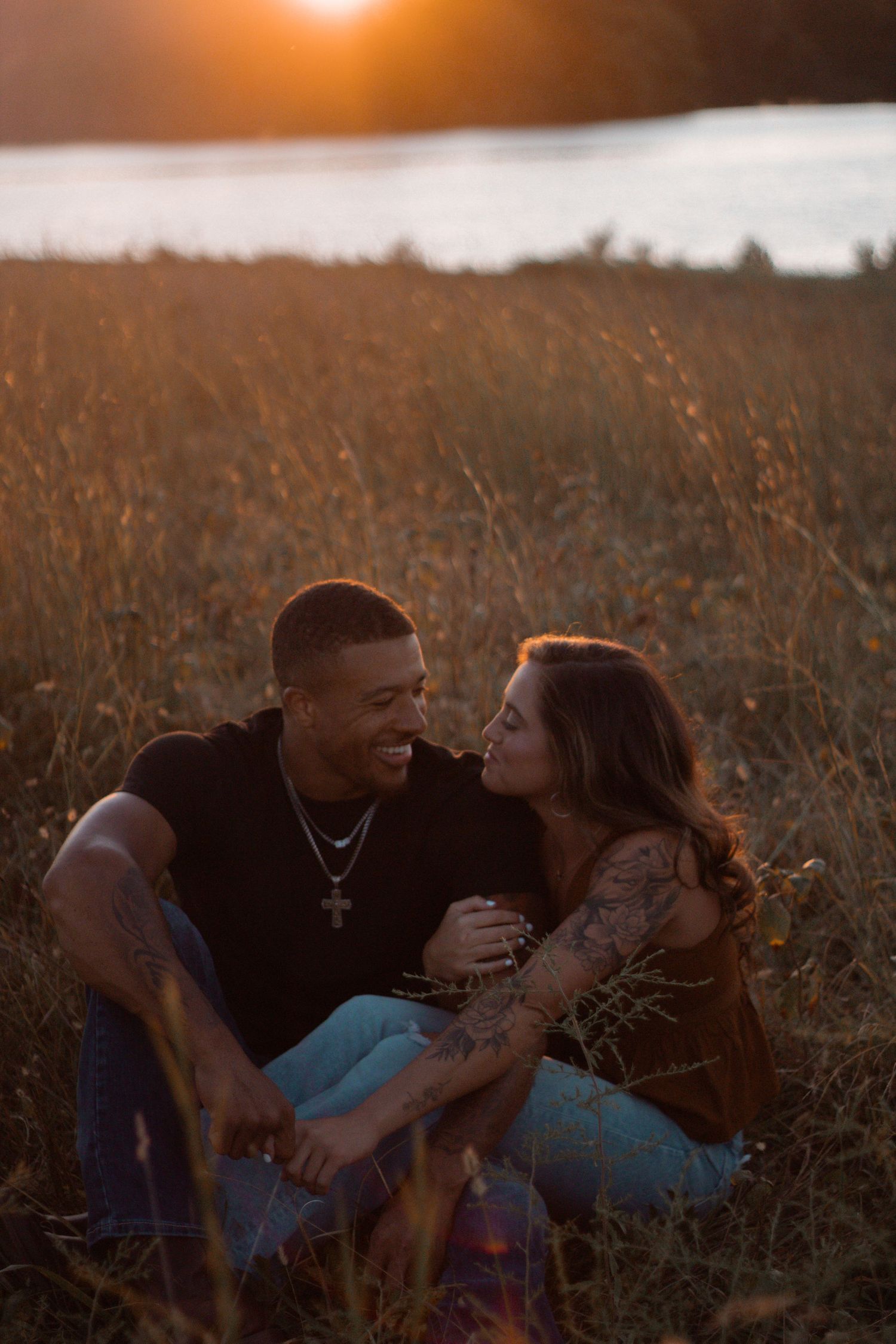 A couple shares an intimate moment lying in a golden field at sunset.