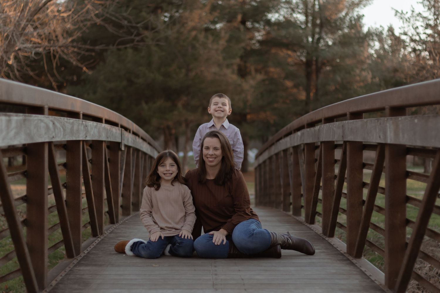 Family sits together on a rustic wooden bridge surrounded by autumn trees during an outdoor photo session.