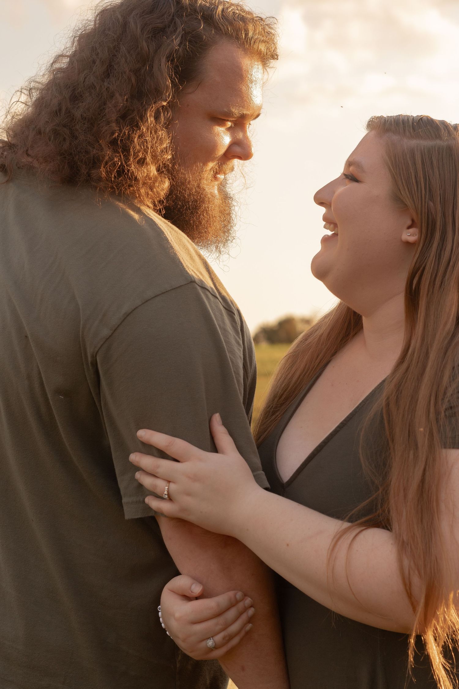 A couple sharing a joyful moment outdoors at golden hour, the woman laughing as they embrace in a sunlit field.