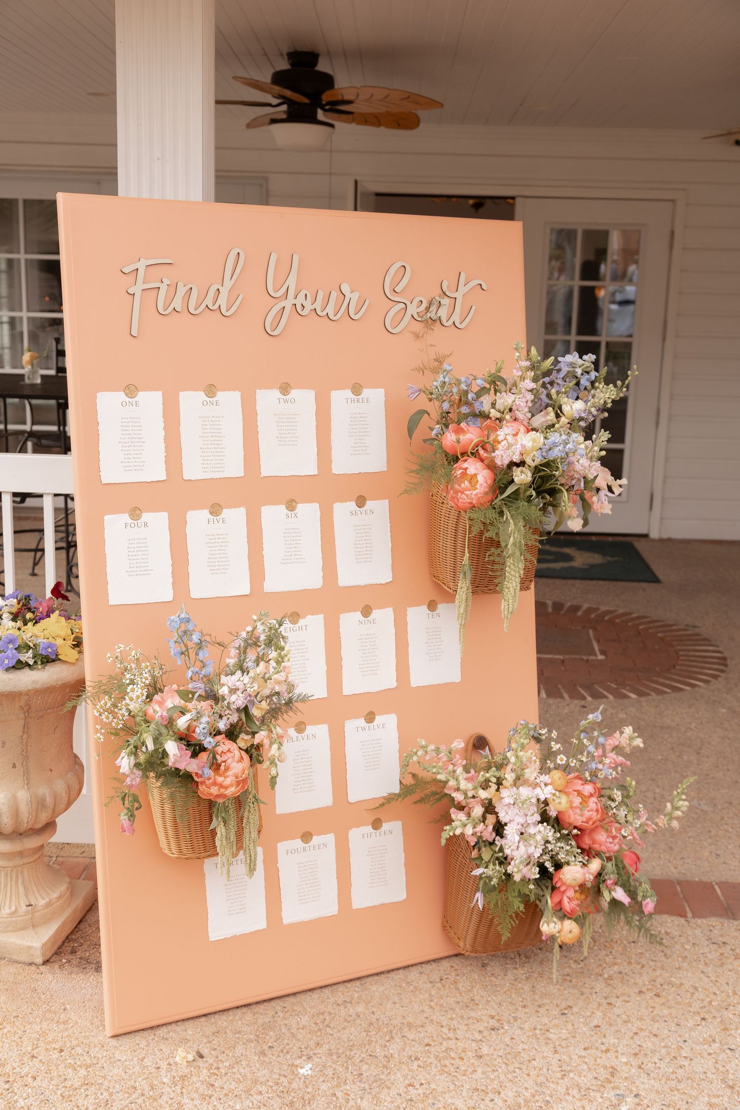 Peach wedding seating chart board with floral arrangements and Find Your Seat sign displaying table assignment cards.