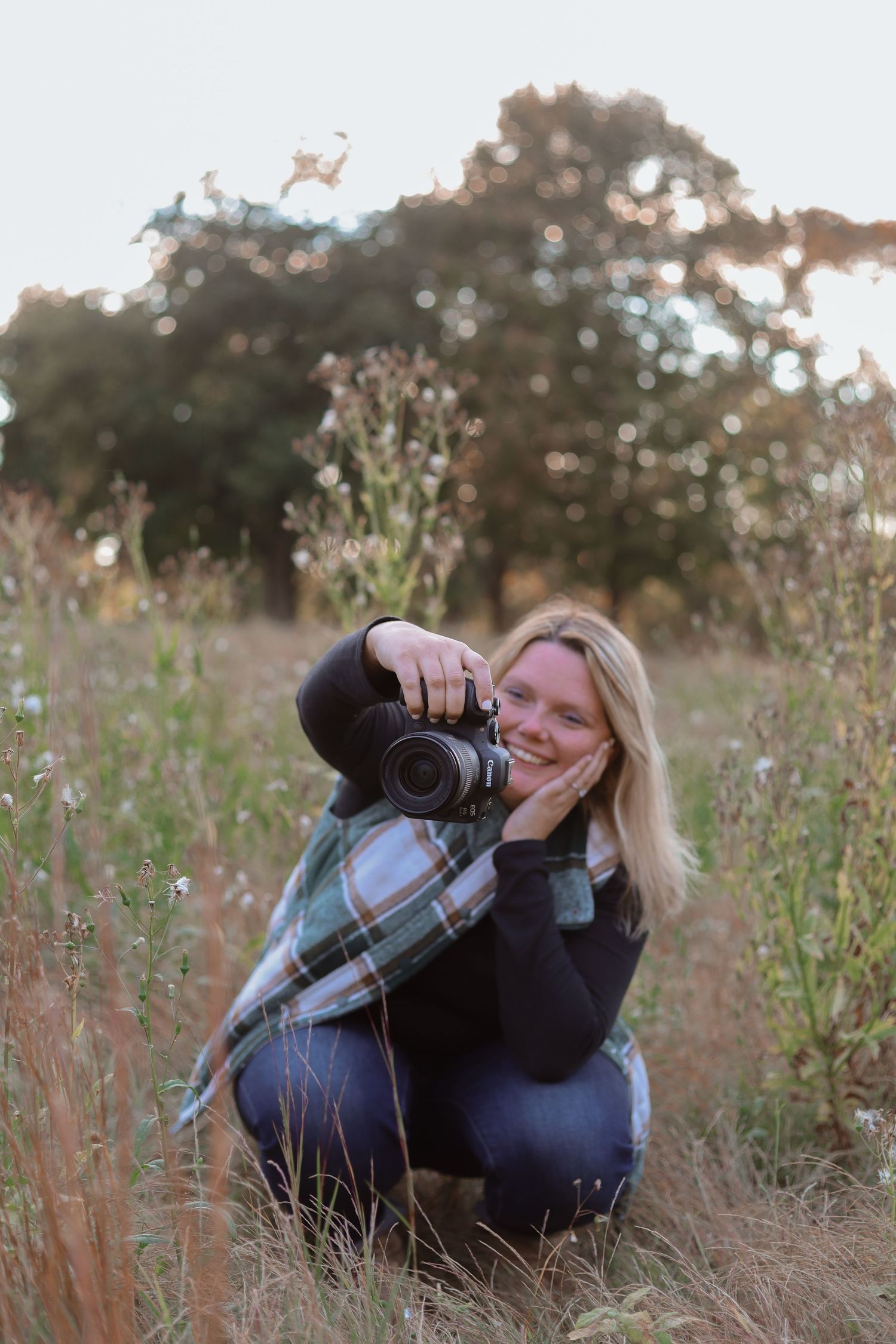 A photographer lies in tall grass at sunset with a professional camera capturing nature shots.