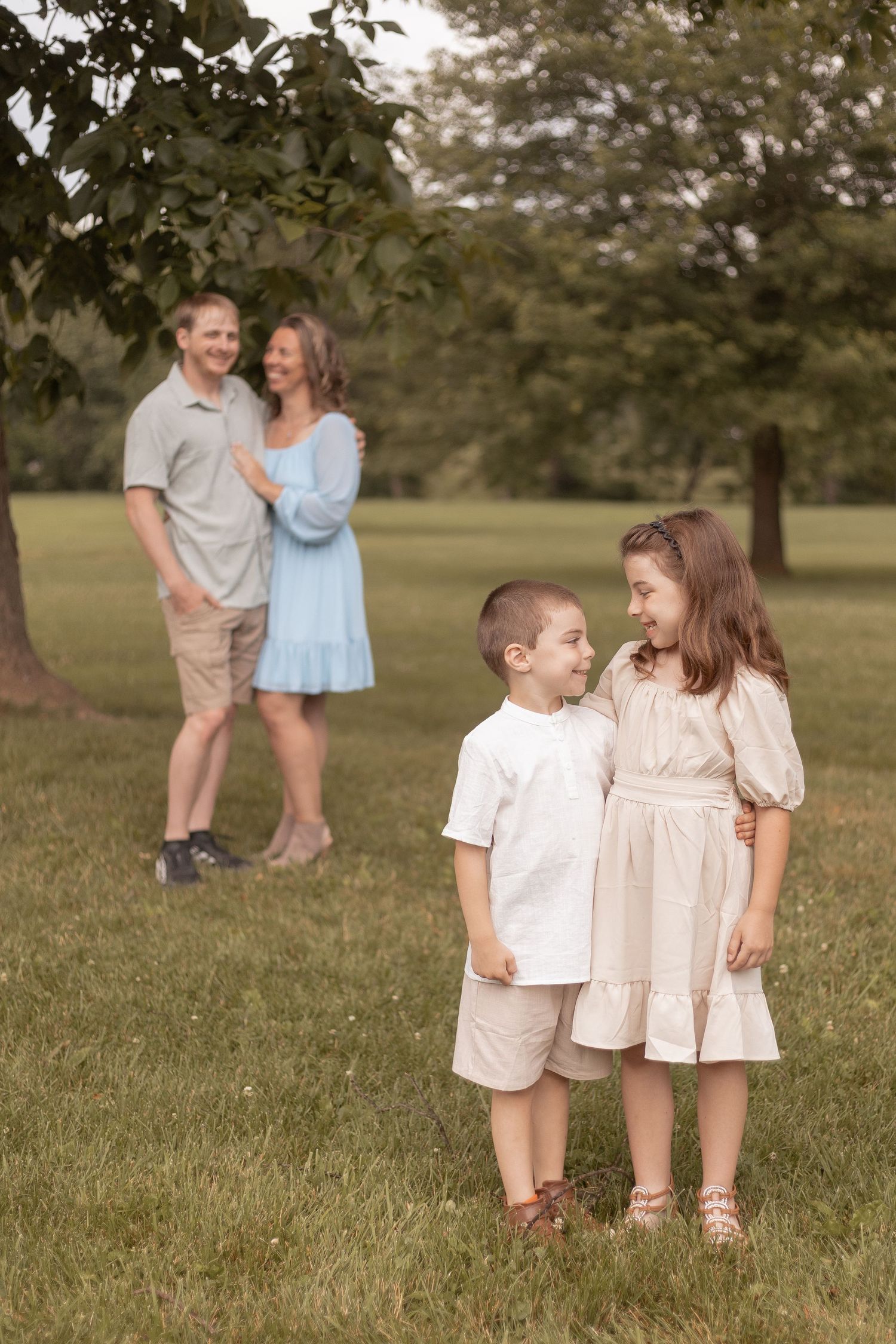 Family portrait with two children smiling in foreground and parents embracing in background on green lawn.