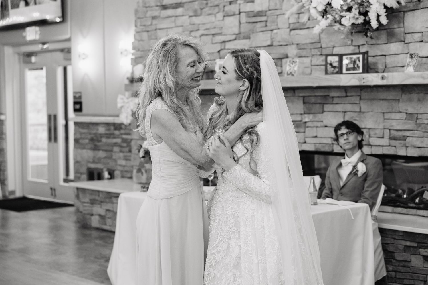 Two brides share a joyful embrace in a black and white wedding photo inside an elegant stone-walled venue.