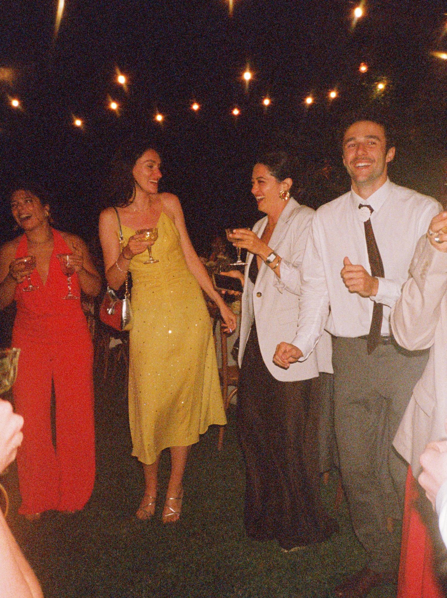 People dancing and celebrating at an outdoor party under string lights in warm evening ambiance.