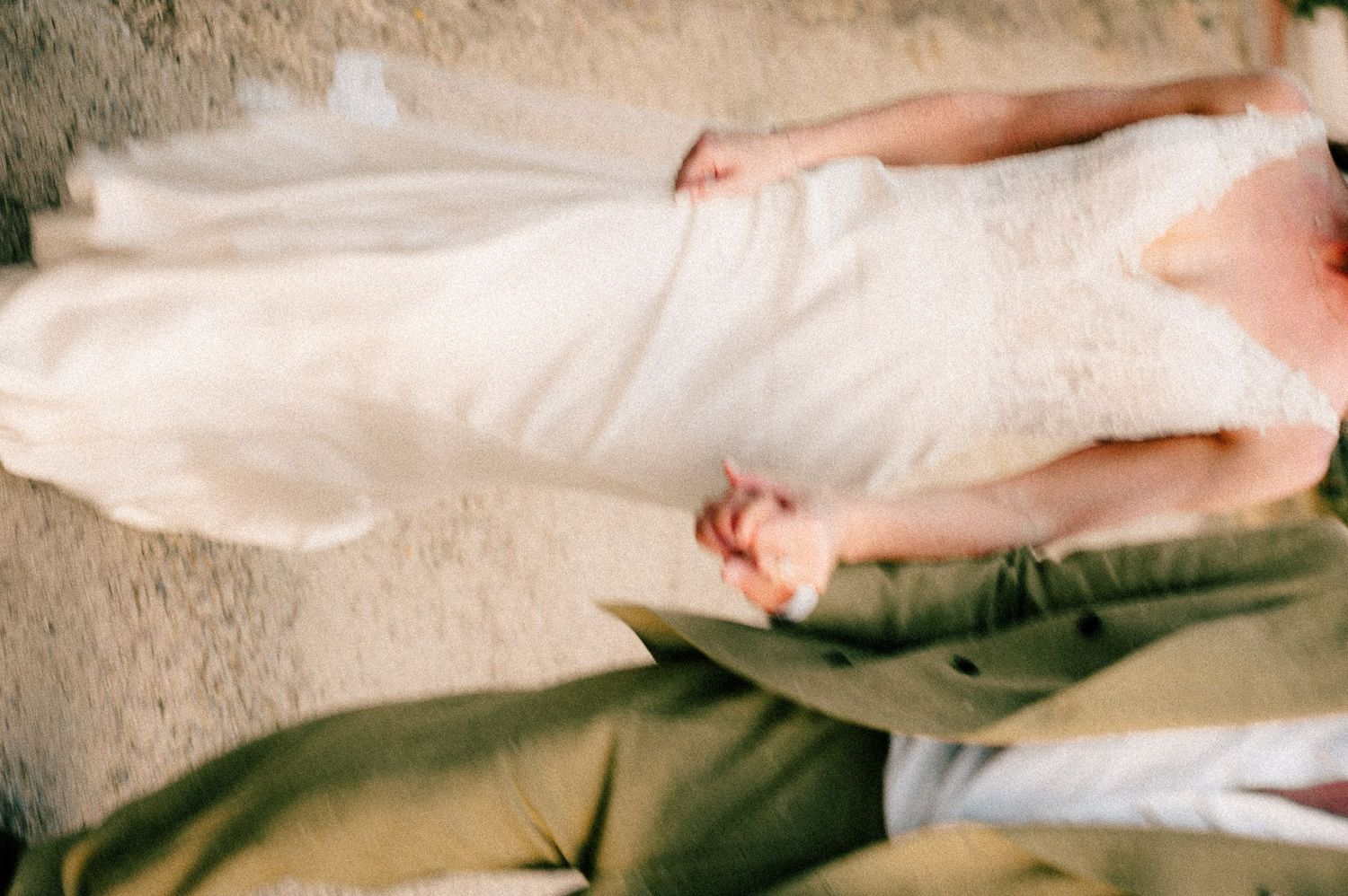 Bride and groom holding hands, wearing white wedding dress and olive green suit at wedding ceremony.