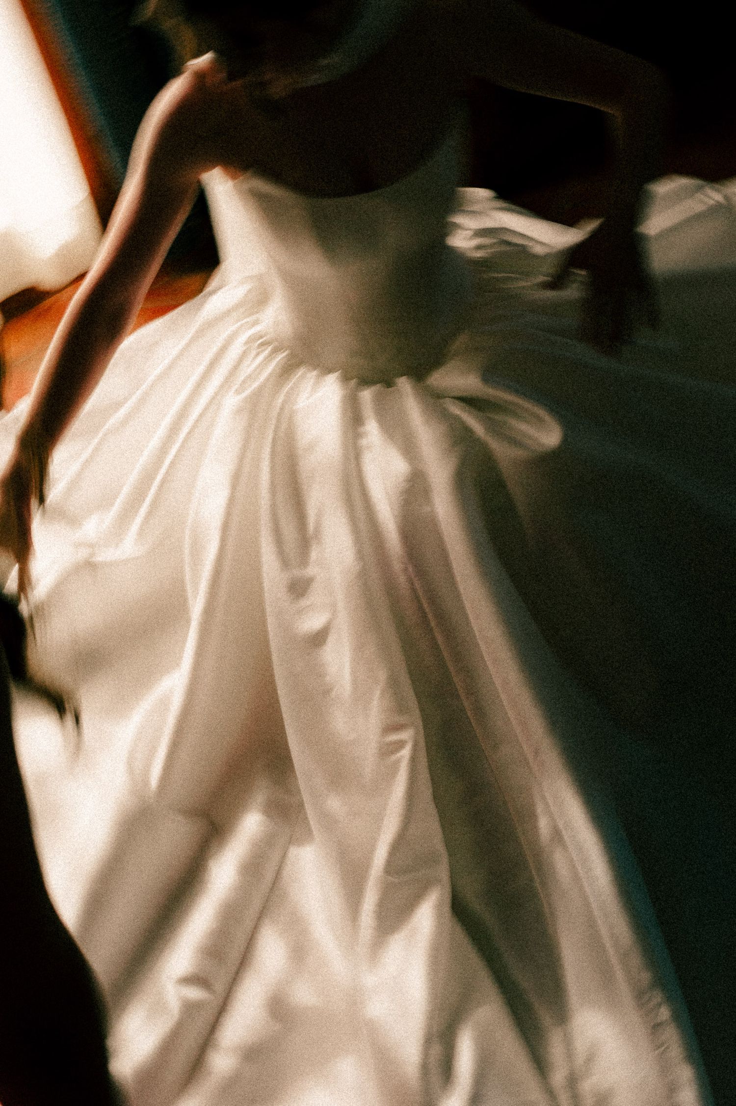 A bride twirls in a voluminous white satin ball gown wedding dress, captured in a dreamy motion-blurred photograph.