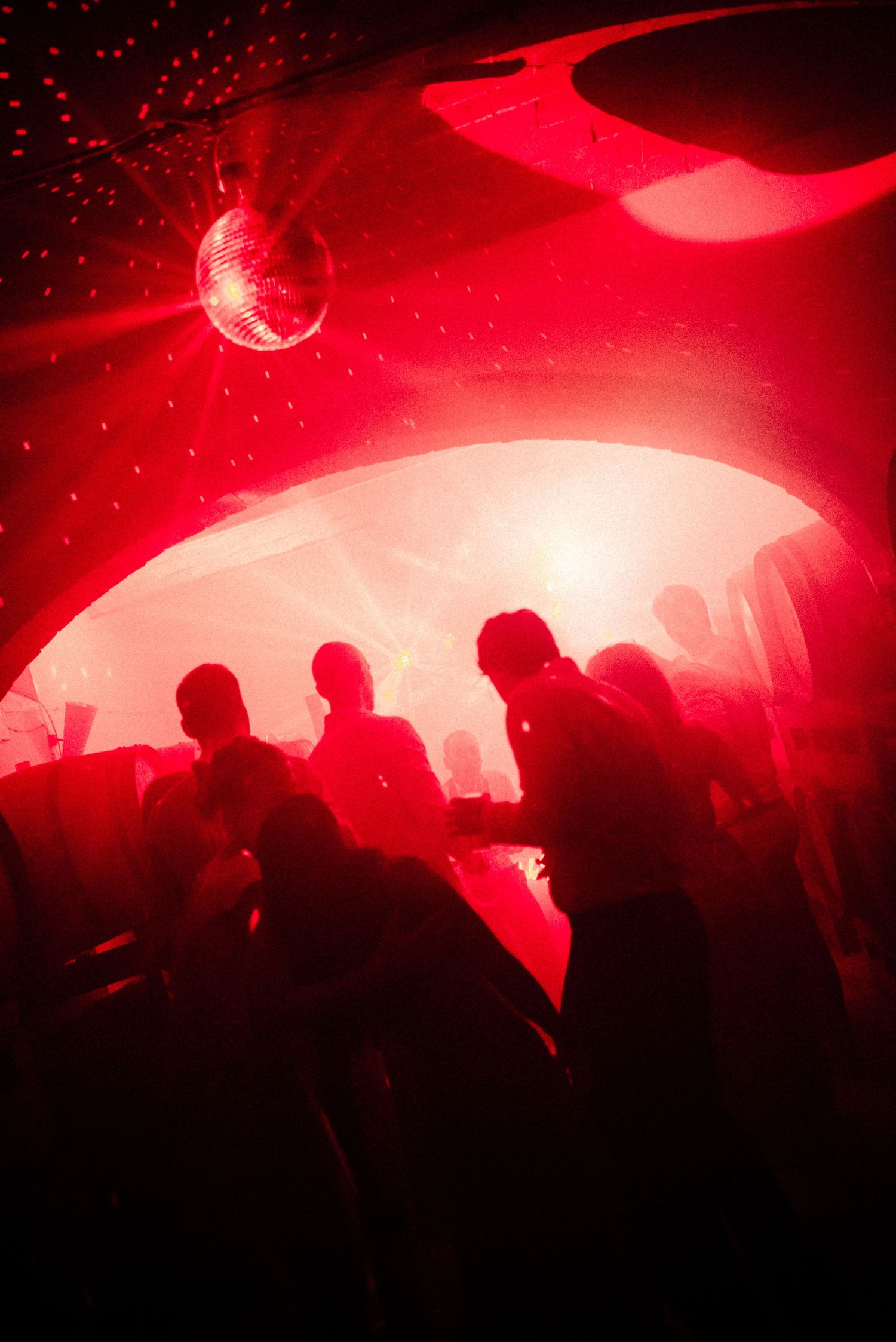 Silhouettes of people dancing in a red-lit nightclub with a disco ball hanging from the ceiling.