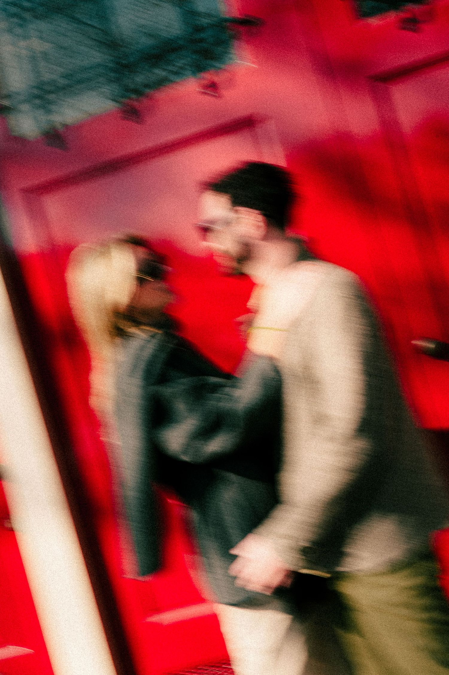 A blurry motion shot of a couple kissing against a vibrant red background in moody, artistic photography.