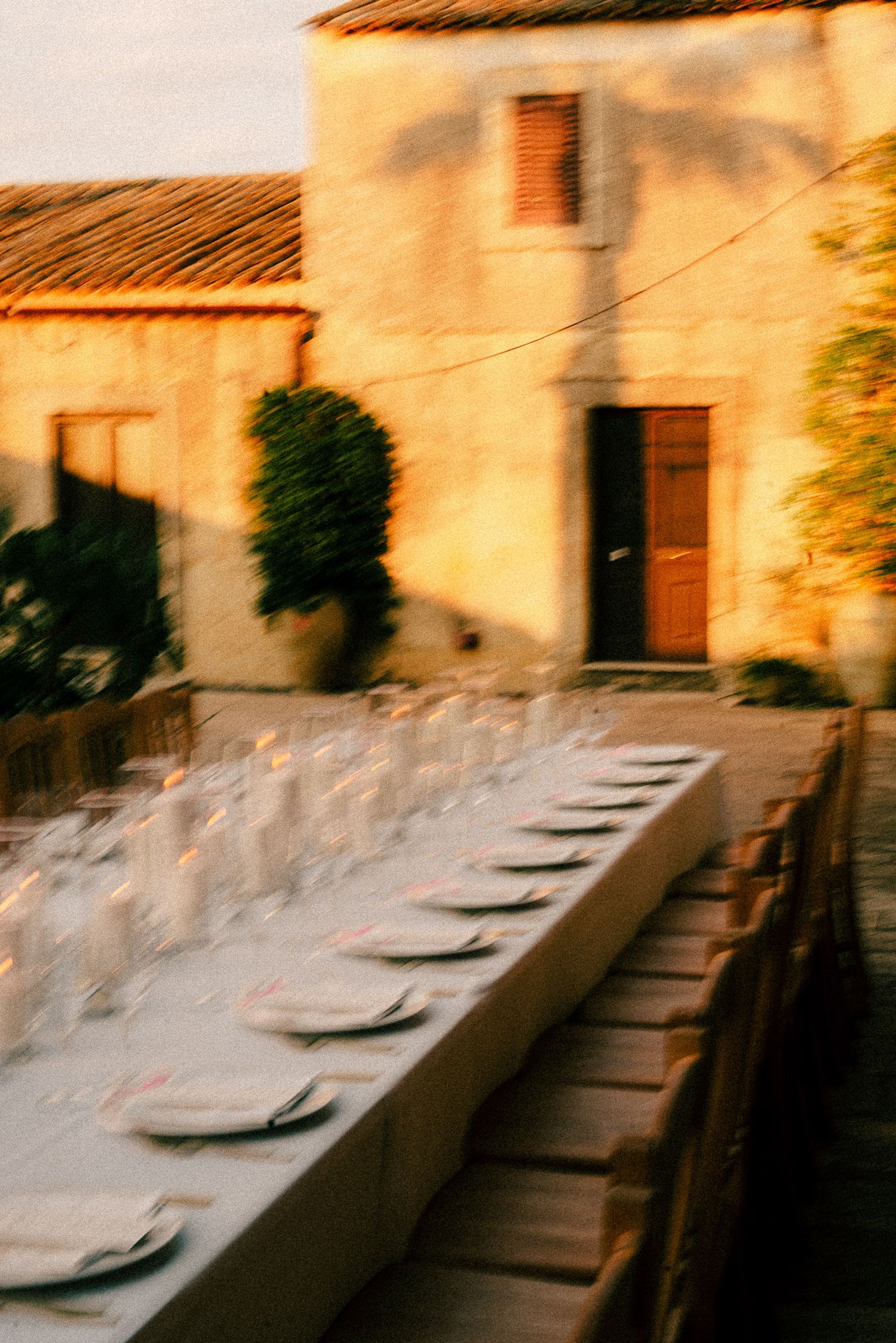 Long outdoor dining table set with glassware at golden hour beside a rustic stone building in Tuscany.